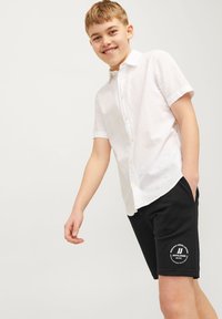 Witte short-sleeve button-up shirt met een zak, gecombineerd met zwarte shorts met een logo-print. Glad textuur, casual ontwerp.