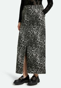 Midi-rok met luipaardprint in grijs en zwart, met een split aan de voorkant en zijzakken. Gepaard met zwarte loafers met dikke zolen.