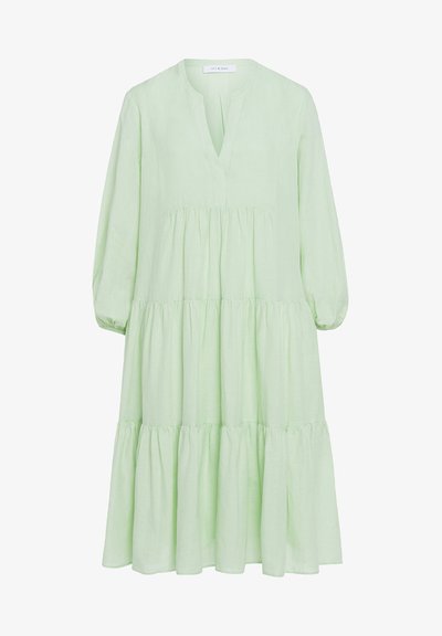 Gaiši zaļš lina kleita ar V-veida kakla izgriezumu, garām pūkainām piedurknēm un slāņotu svārku. Atbrīvota piegriezuma ar mīkstu tekstūru un smalkiem pludinājuma elementiem.