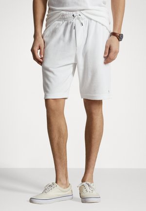 Shorts en coton blancs avec une taille élastique et un cordon de serrage. Présente une texture lisse et des poches latérales. Associés à des baskets de couleur claire.