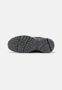 Musta New Balance -lenkkarien pohja, jossa on teksturoitu kulutuspinta ja tuotemerkki näkyvissä kannassa ja välipohjassa.