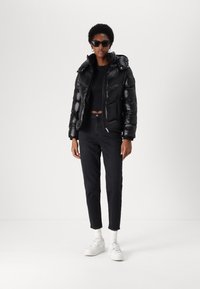 Black puffer jacket with a glossy finish, padded design, adjustable hood, and zip closure, paired with black jeans and white sneakers.