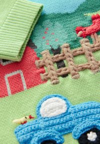 Pletená sveterová sekcia s zeleným základom, viacfarebnou farmárskou scénou s výšivkami: červená stodola, hnedý plot, modrý traktor a vtáky.