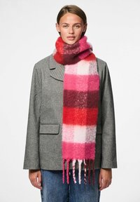 Sciarpa a quadri multicolore nelle tonalità di rosa, rosso e bianco, realizzata in un tessuto morbido e texture con estremità frangiate. Indossata con un blazer grigio.