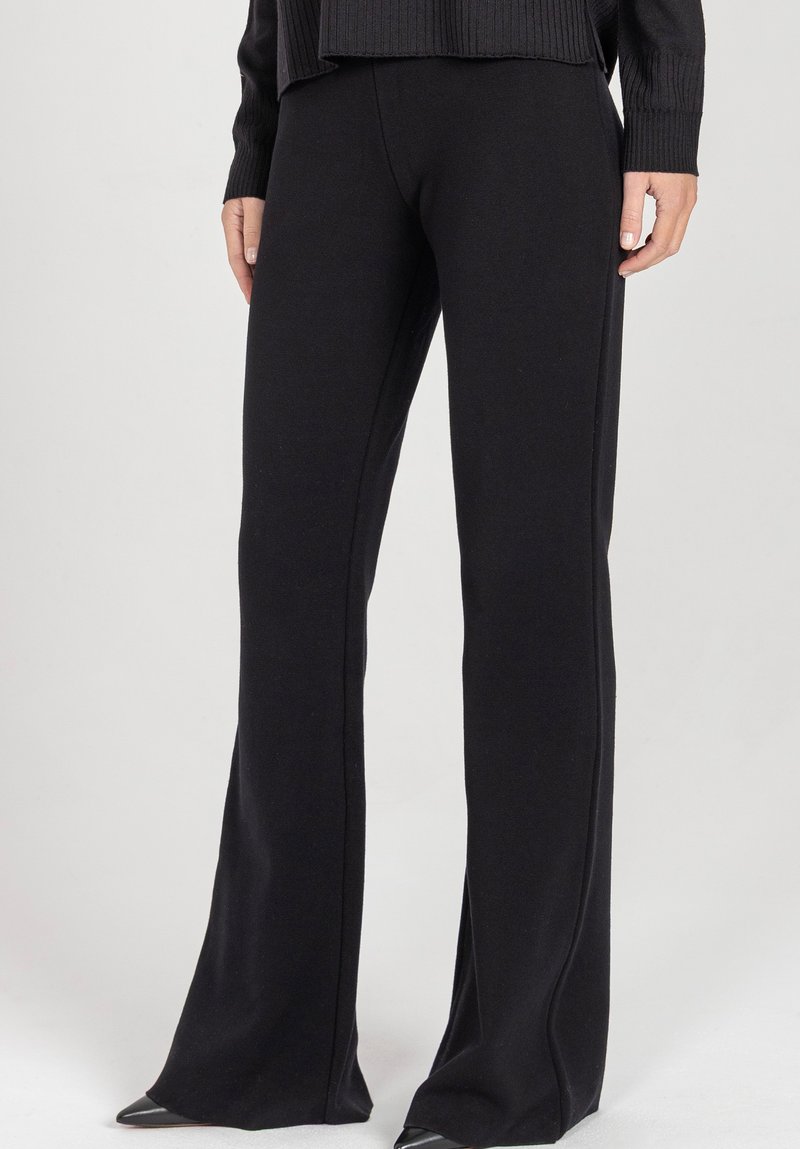 Czarne rozszerzane spodnie z miękkiego materiału. Posiadają przeszycia wzdłuż szwów, tworząc gładką sylwetkę.
