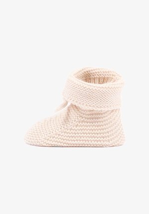 Kremowy ręcznie robiony, dziany bucik dziecięcy z podwiniętą mankietem, miękką, fakturowaną przędzą i prostym wzorem na białym tle.