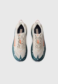 Lichte hardloopschoenen in crème en teal, met een patroon op de bovenkant, oranje merkvermelding, een gevoerde zool en contrasterende accenten.