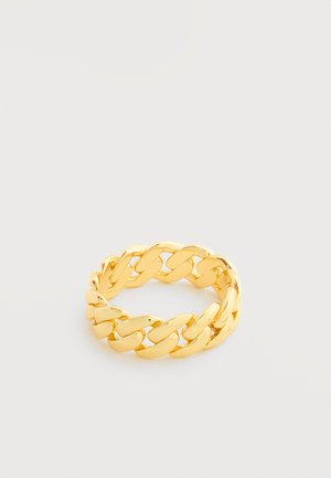 Arany láncszem gyűrű fehér felületen, vastag, összekapcsolódó, ívelt szemekkel és polírozott felülettel.