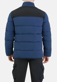 Giacca puffer blu navy con pannello superiore nero, caratterizzata da un design trapuntato, colletto alto e polsini elastici. La vista posteriore mostra una texture liscia.