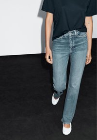 T-shirt bleu foncé ajusté associé à un jean droit bleu clair. Ballerines blanches avec un accent circulaire. Texture en denim lisse et design décontracté.