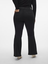 Zwarte uitlopende spijkerbroek met een gladde textuur, achterzakken en een getailleerde taille, gecombineerd met lichtgekleurde hakken voor contrast tegen de zwarte stof.