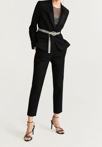 Czarny, dopasowany garnitur z wąskimi spodniami, z metalowym paskiem, przezroczystą czarną bluzką i czarnymi, sandałowymi szpilkami. Gładki materiał, wyrafinowany krój.