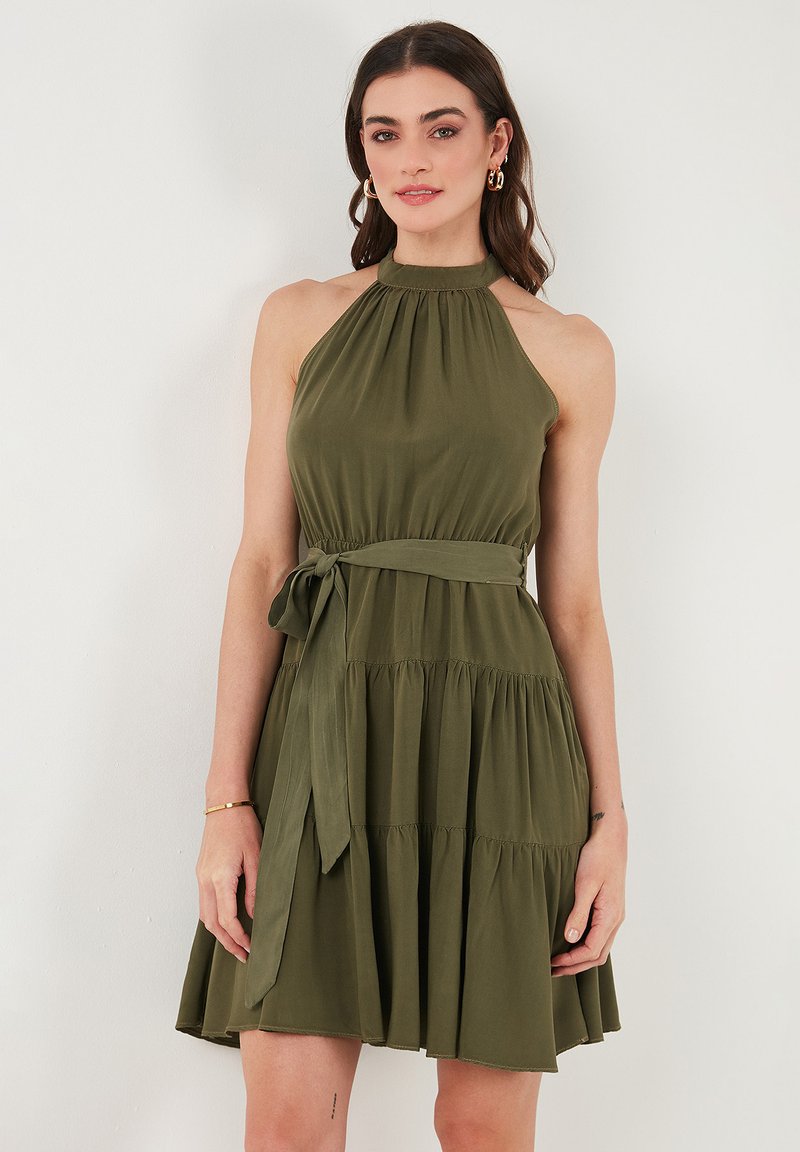 Abito halter verde oliva realizzato in tessuto leggero, con corpino aderente, gonna a strati e cintura da annodare in vita.