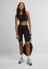 Svart atletisk crop-top og sykkelshorts, laget av elastisk materiale. Båret med grå sneakers og en svart snorveske. Hvite sokker synlige.