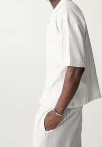 Chemise blanche à manches courtes avec des rayures verticales, dotée d'un col et de boutons. Associée à un pantalon assorti, présentant une coupe décontractée et des poches.