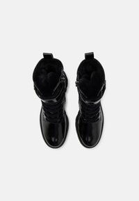 Paire de bottes noires brillantes à lacets, doublées en fourrure avec fermetures éclair latérales, vues de dessus sur un fond blanc.