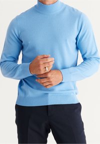 Ljusblå stickad polotröja med ribbade ärmslut och nederkant. Tätt sittande design med långa ärmar. Slät textur, bärs med mörka byxor.
