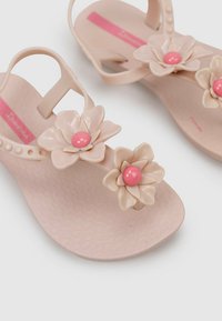 Sandalias de gel rosa claro con adornos florales, que cuentan con suelas suaves y texturizadas y perlas rosas en el centro de cada flor.