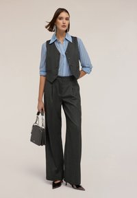 Grijze gebonden gepersonaliseerde vest gecombineerd met een lichtblauw gestreept overhemd en brede grijze broek. Accessoires omvatten een kleine handtas.