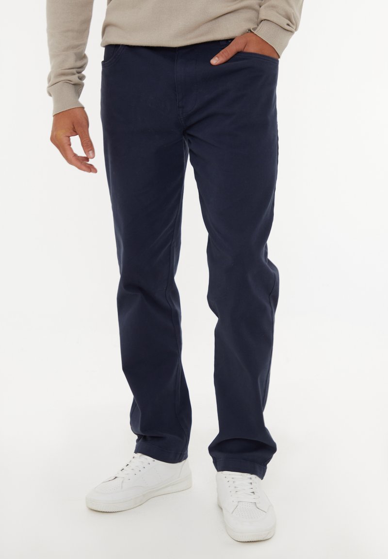 Marineblaue Chinos aus Baumwolle mit geradem Bein, ausgestattet mit Seitentaschen und einem lässigen Schnitt, kombiniert mit weißen Sneakers.