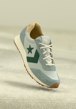 Light blue sneakers with gray suede accents, green star and chevron design, cream laces, tan inner lining, and textured brown outsole.