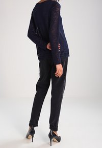 Marinblå stickad tröja med öppen vävdetalj vid fållarna, i kombination med svarta tapered byxor och högklackade skor. Texturerad tyg synligt.