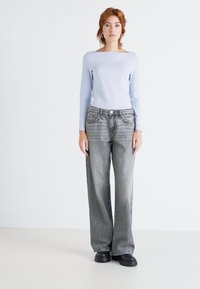 Lyseblå langermet topp, grå bredbeinede jeans med falmet tekstur, og svarte plattformsko, mot en enkel hvit bakgrunn.