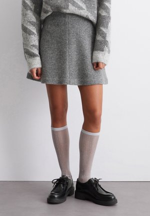 Grå uldnederdel kombineret med en grå og hvid mønstret sweater. Supplerende elementer: knæhøje skinnende sokker og sorte plateau sko.