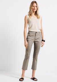 Haut sans manches beige en maille texturée, associé à un pantalon gris cropped avec poches avant, passants de ceinture et un design épuré. Des sandales noires sont portées.