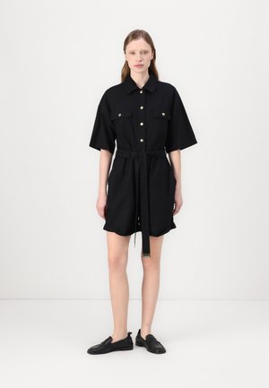 Rochie neagră cu mânecă scurtă, guler, închidere cu nasturi pe față, două buzunare pe piept, talie strânsă cu o curea și un material textil neted.