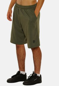 Olivgrüne Shorts mit einem elastischen Bund, seitlichen Taschen und einem schwarzen Logo-Accent. Hergestellt aus einem weichen, leichten Stoff.