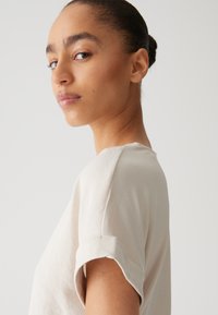 Hellbeige Kurzarmhemd mit umgeschlagenen Ärmeln, aus weichem Material, mit Rundhals und lässiger Passform. Minimalistisches Design.