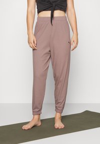 Braune Ripp-Jogginghosen mit einem elastischen Bund, schmal zulaufenden Knöcheln und einem kleinen Logo an der Seite, kombiniert mit einem schwarzen, kurz geschnittenen Oberteil.