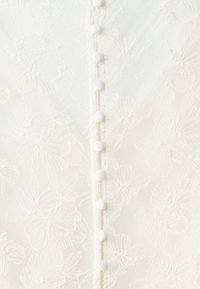 Kantstof met bloemmotief in het wit, met een centrale rij van zes witte ronde knopen langs de voorkant. Textuur en doorzichtig uiterlijk.