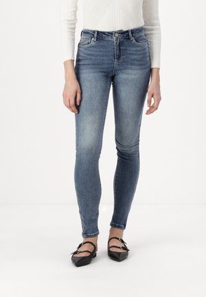 Skinny jeans in medium blue denim, featuring a high waist, slight whiskering, and minimal fading. Paired with black flats.