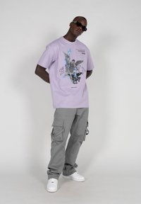 Lavendel grafisk t-shirt med et detaljeret design på fronten, parret med grå cargo bukser med flere lommer og en afslappet pasform.