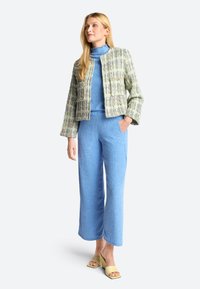 Light green and white patterned tweed jacket with two pockets, paired with a blue turtleneck and wide-leg blue trousers. Yellow slide sandals.