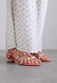 Rosa klacksandaler med flerfärgade, mönstrade remmar. Klacken har en zickzackdesign. Matchas med ett texturerat vitt plagg.