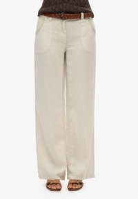 Pantaloni larghi in lino color beige chiaro con due tasche laterali e una cintura intrecciata marrone. Tessuto morbido e vestibilità casual.
