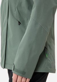 Groene waterdichte jas met een gladde textuur, verstelbare manchetten met klittenband en een klein logoaccent op de zijnaad.