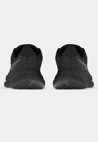 Aknad mustad sportlikud jooksujalatsid kirju vahevahuga, nähtavad tagant, lihtsa valge taustal.