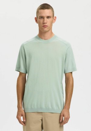 Gaiši zaļš adīts īsroku džemperis ar apaļu kaklu, ribotu apkakli un brīvu pieguvumu. Gluda tekstūra, ikdienišķs dizains.