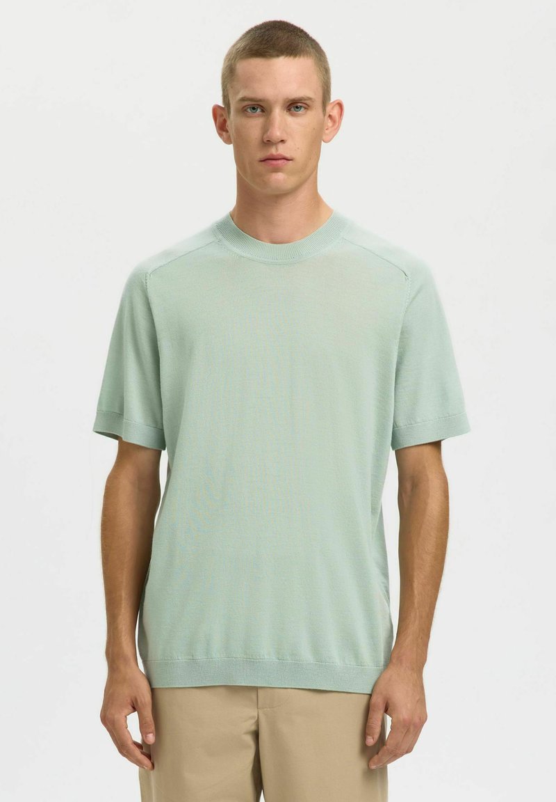 Pull court à manches courtes en tricot vert clair avec col rond, encolure côtelée et coupe décontractée. Texture lisse, design décontracté.