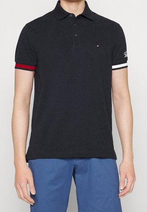 Sort polo skjorte med tre-knap lukning, kontrasterende røde og hvide striber på ærmerne og et lille logo på brystet.