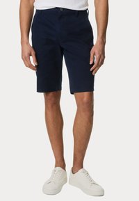 Pantaloni corti blu navy in misto cotone, con taglio dritto, passanti per cintura, tasche frontali e chiusura con un singolo bottone. Abbinati a sneakers bianche.