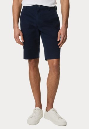 Marineblå shorts lavet af en bomuldsblanding, med lige snit, bæltestropper, forlommer og en enkelt knaplukning. Kombineret med hvide sneakers.