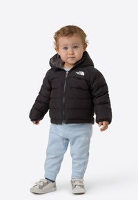 Czarna pikowana kurtka puchowa z kapturem, szara podszewka, w zestawie z jasnoniebieskimi dresami oraz szarymi butami na rzepy.