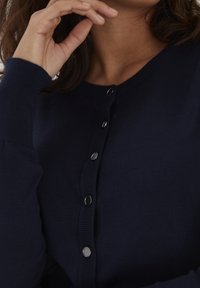 Cardigan lavorato a maglia blu navy con scollo rotondo, maniche lunghe e chiusura frontale con cinque bottoni metallici. Morbida al tatto, con polsini a coste.