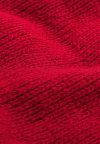 Czerwona dziana tkanina o fakturowanym wzorze, z miękkimi włóknami i falistym wyglądem, podkreślająca ciepło i głębię koloru.