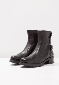 Svarta läderankelstövlar med dragkedjestängning, platt sula och ett dekorativt sidorems. Slät textur och rundad tådesign.